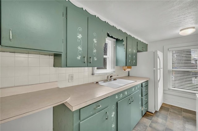 kitchen featuring a sink, tasteful backsplash, freestanding refrigerator, and green cabinetry