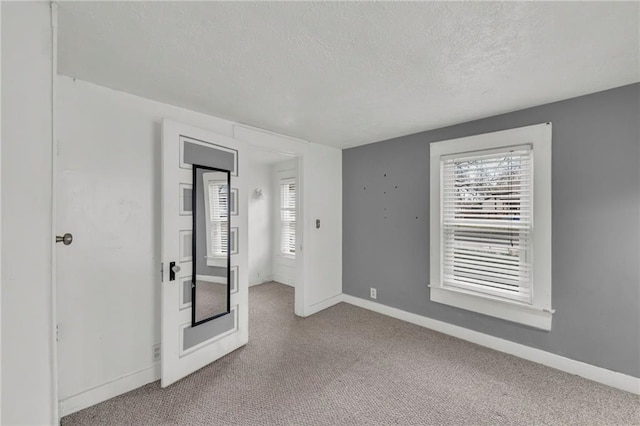 unfurnished bedroom featuring multiple windows, carpet, a textured ceiling, and baseboards