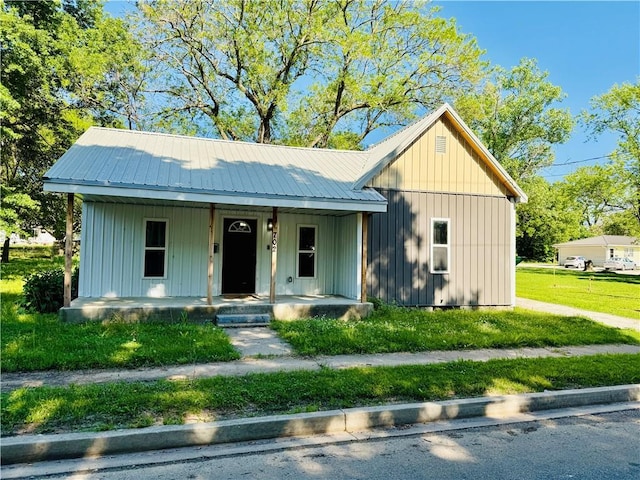 702 N Cedar St, Nevada, MO 64772 - view of front facade featuring covered porch, board and batten siding, a metal roof, and a front lawn