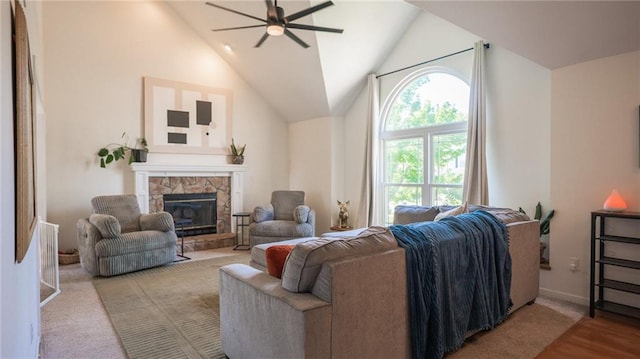 living area with ceiling fan, a stone fireplace, vaulted ceiling, baseboards, and wood finished floors