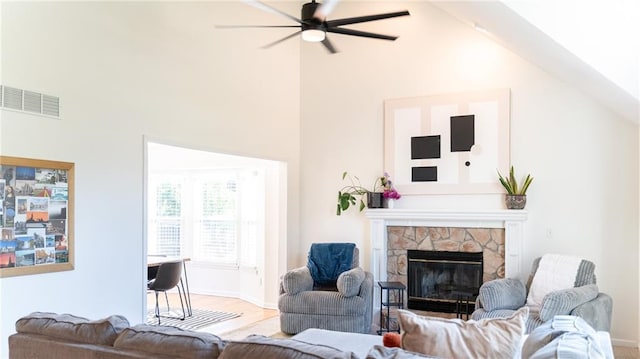 living area with a ceiling fan, a stone fireplace, wood finished floors, baseboards, and high vaulted ceiling