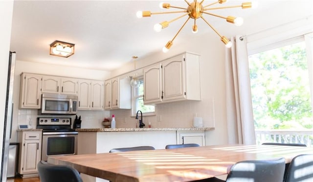 kitchen with appliances with stainless steel finishes, backsplash, and a chandelier