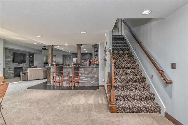 4502 Verona Ct, Riverside, MO 64150 - staircase featuring carpet flooring, ceiling fan, a large fireplace, decorative columns, and baseboards