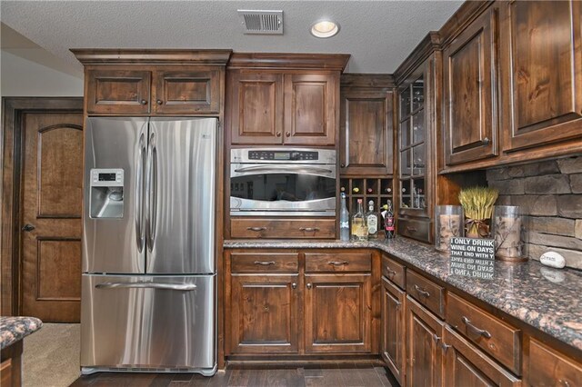 4502 Verona Ct, Riverside, MO 64150 - kitchen with appliances with stainless steel finishes, a textured ceiling, dark stone countertops, and dark brown cabinets