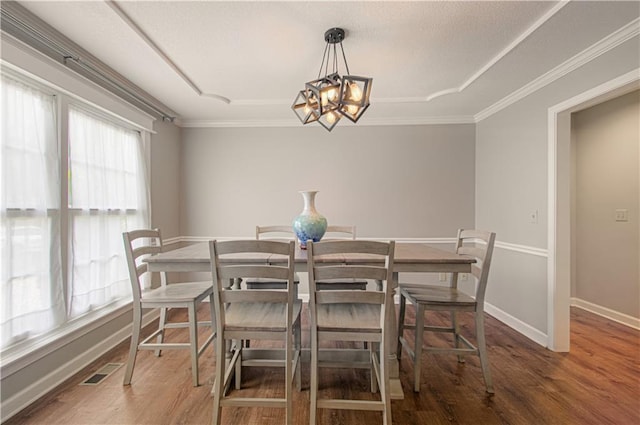 dining space featuring wood finished floors, a chandelier, baseboards, crown molding, and a raised ceiling