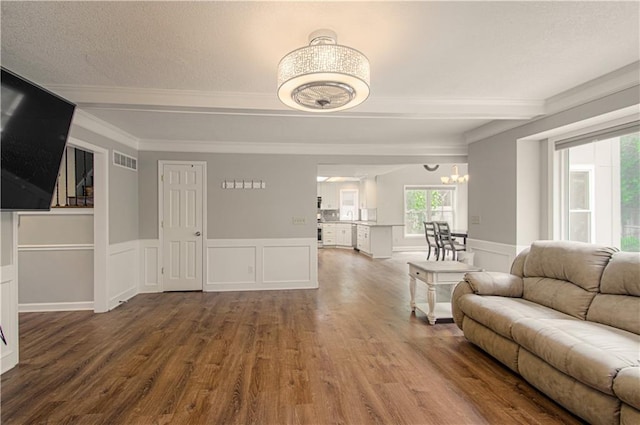 living area with crown molding, wood finished floors, a wainscoted wall, a chandelier, and a decorative wall