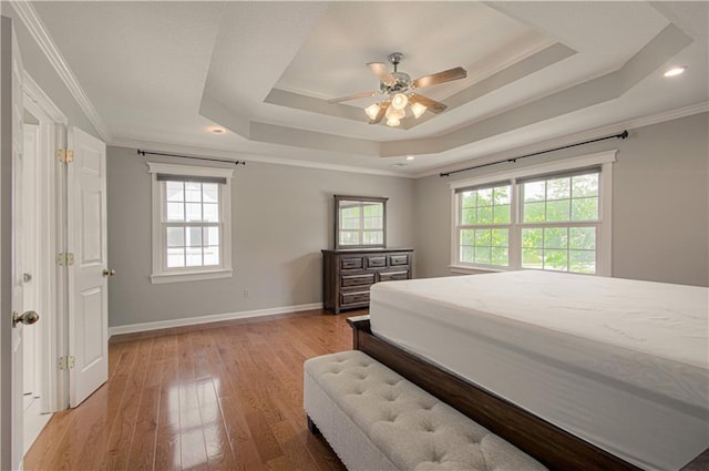 bedroom with a tray ceiling, multiple windows, baseboards, light wood-style floors, and crown molding