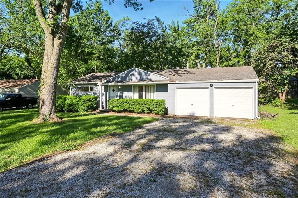 8306 James A Reed Rd, Raytown, MO 64138 - view of front of home with an attached garage, a front lawn, and gravel driveway