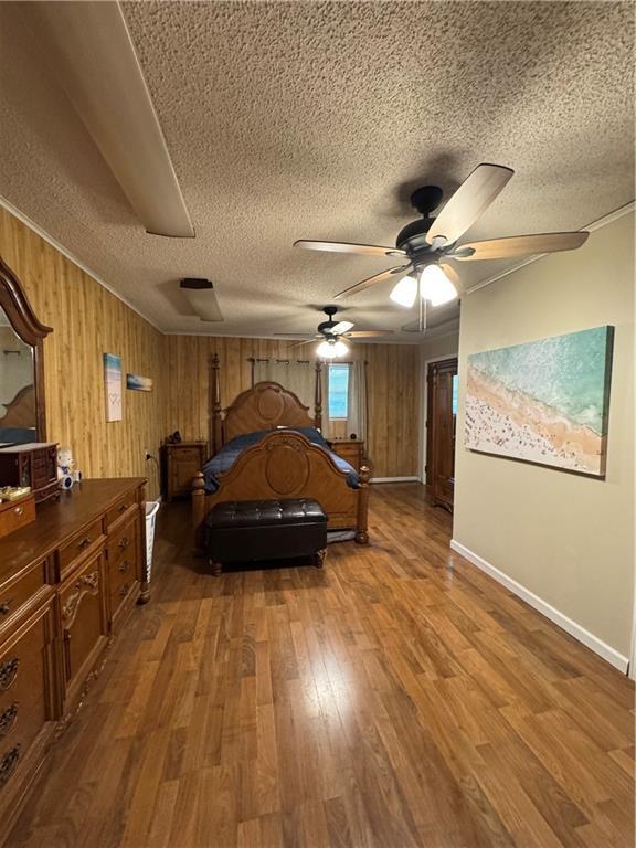 209 S 4th St, Arma, KS 66712 - bedroom featuring wood finished floors, a textured ceiling, baseboards, and wood walls