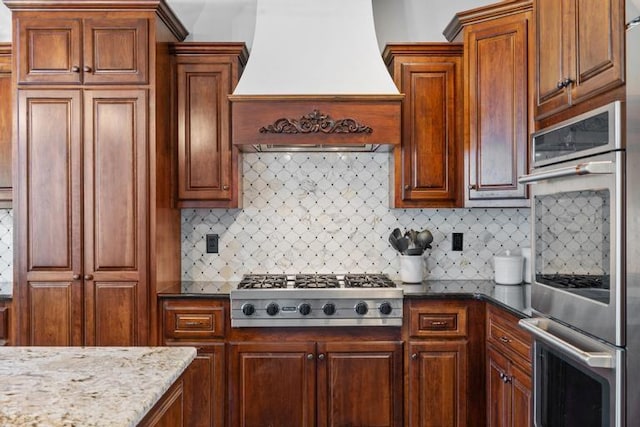 8127 Lone Elm Rd, Lenexa, KS 66220 - kitchen featuring wall chimney exhaust hood, stainless steel appliances, decorative backsplash, dark stone countertops, and brown cabinetry