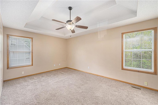 spare room featuring a raised ceiling, carpet, baseboards, ceiling fan, and a textured ceiling