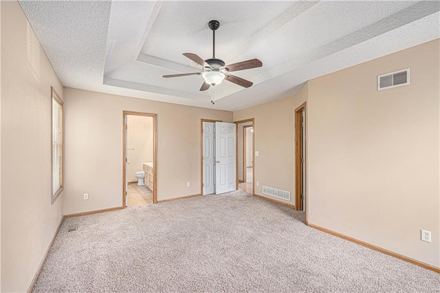 unfurnished bedroom with light carpet, baseboards, ensuite bath, a textured ceiling, and a tray ceiling