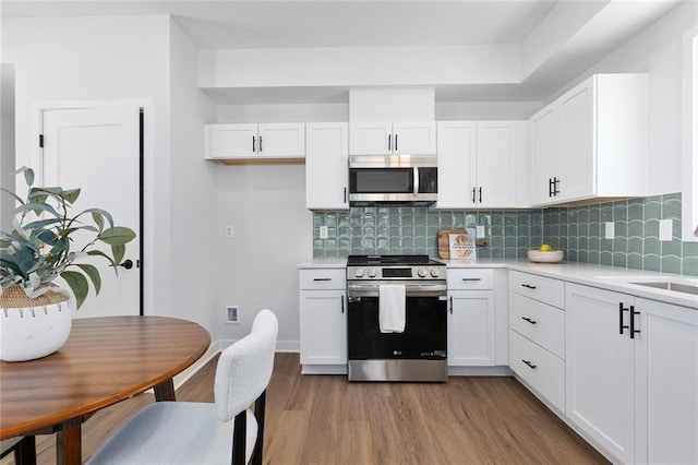 kitchen with stainless steel appliances, light countertops, wood finished floors, and white cabinetry