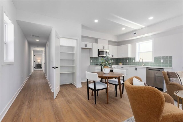 kitchen featuring appliances with stainless steel finishes, light wood-style flooring, white cabinetry, light countertops, and decorative backsplash