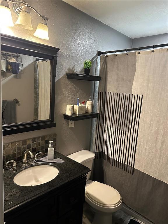 full bath featuring a textured wall, toilet, vanity, and decorative backsplash