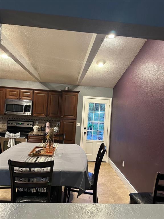 dining space with vaulted ceiling, light tile patterned floors, baseboards, and a textured ceiling