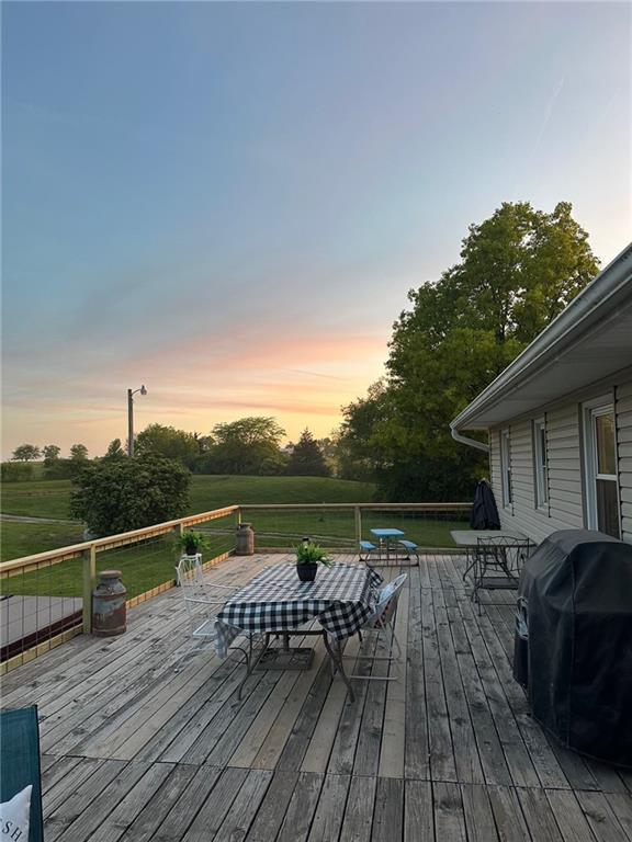deck at dusk featuring a lawn and grilling area