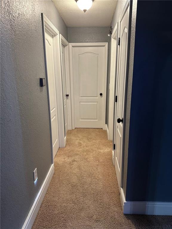 hallway with a textured wall, light colored carpet, and baseboards