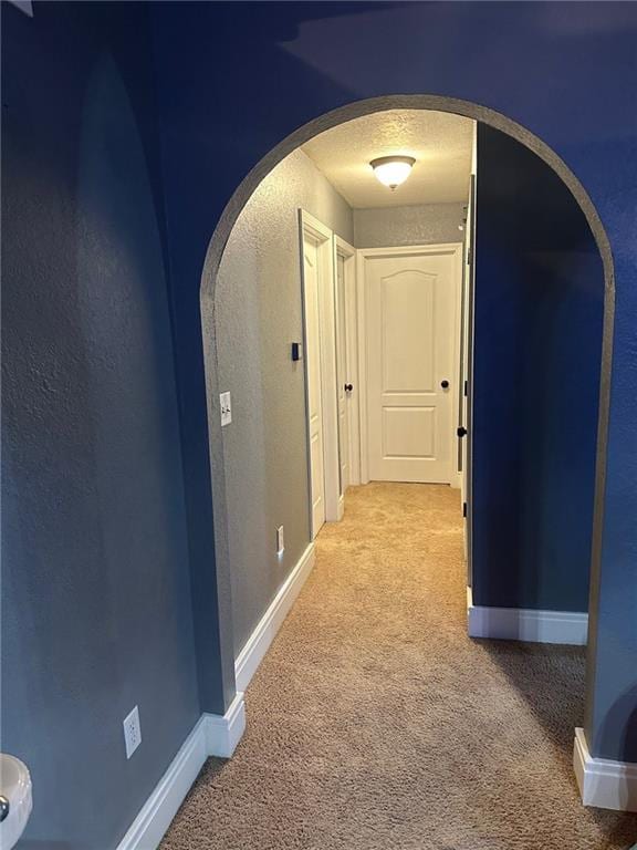 corridor with arched walkways, carpet, and baseboards