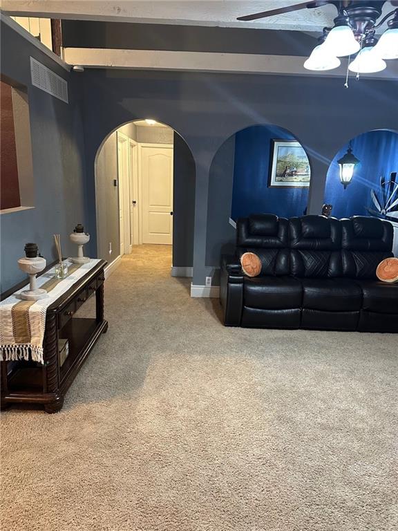 carpeted home theater with arched walkways, a ceiling fan, beamed ceiling, and baseboards