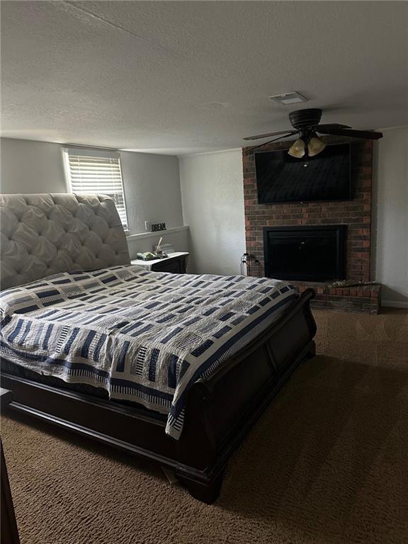bedroom with carpet, a brick fireplace, and a textured ceiling