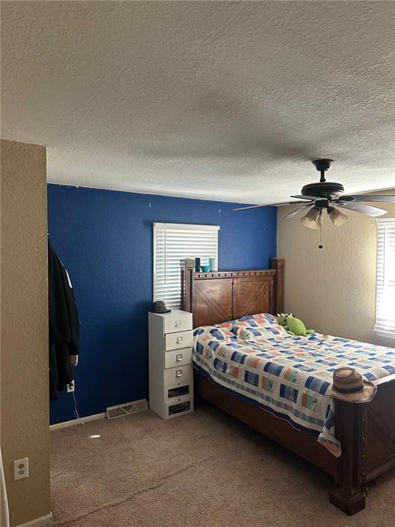 carpeted bedroom featuring multiple windows, a textured ceiling, a textured wall, ceiling fan, and baseboards