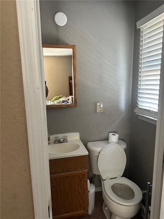 bathroom with toilet, vanity, and a textured wall