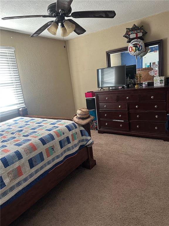 bedroom with light colored carpet, multiple windows, a textured ceiling, and ceiling fan
