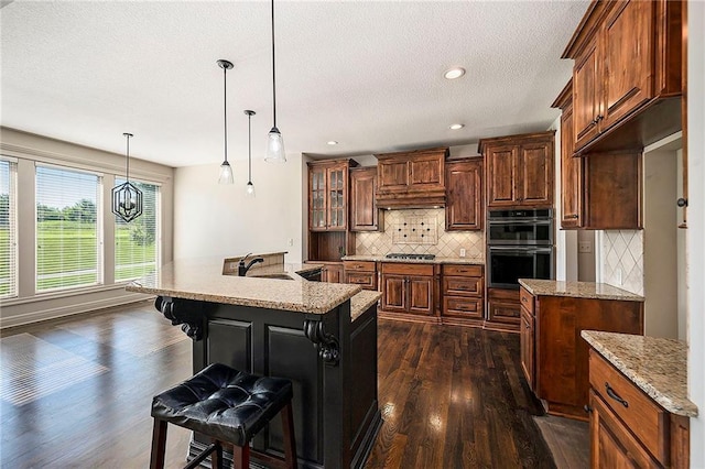 4301 N 141st St, Basehor, KS 66007 - kitchen with dark wood-style floors, stainless steel gas stovetop, decorative backsplash, a breakfast bar area, and an island with sink