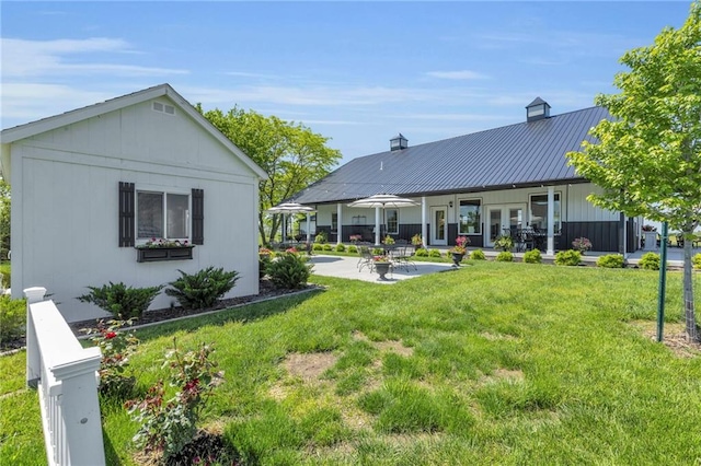 rear view of property featuring a yard, a patio area, metal roof, a chimney, and a standing seam roof