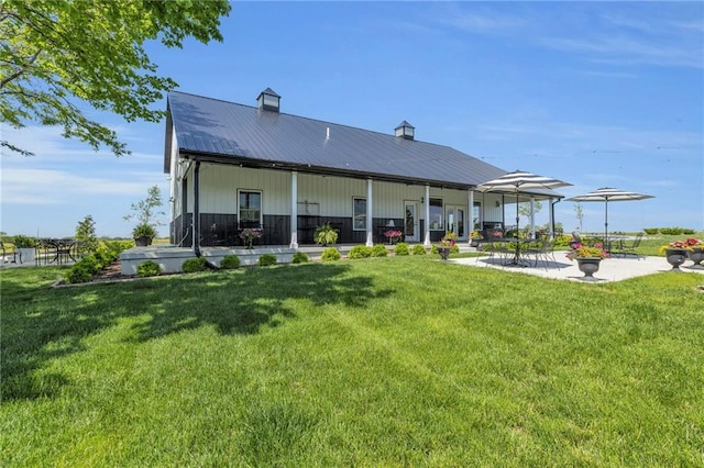 rear view of property featuring a chimney, a lawn, metal roof, and a patio area