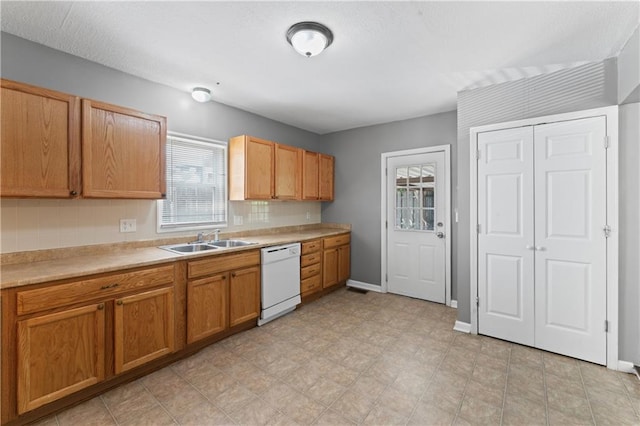 kitchen with white dishwasher, a sink, light countertops, decorative backsplash, and baseboards