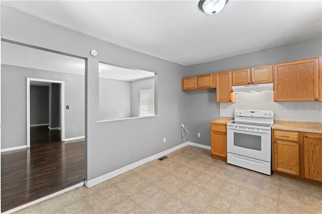 kitchen with white range with electric stovetop, under cabinet range hood, light countertops, backsplash, and baseboards