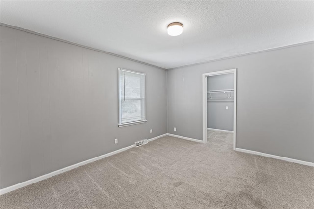 unfurnished bedroom featuring a textured ceiling, carpet flooring, baseboards, a spacious closet, and a closet