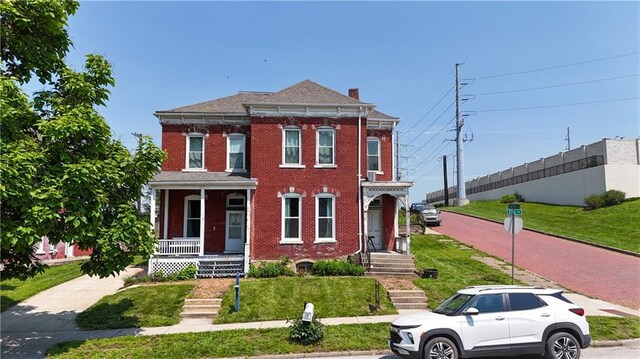 432 S 5th St, Atchison, KS 66002 - view of front of property with covered porch, brick siding, a chimney, and a front lawn