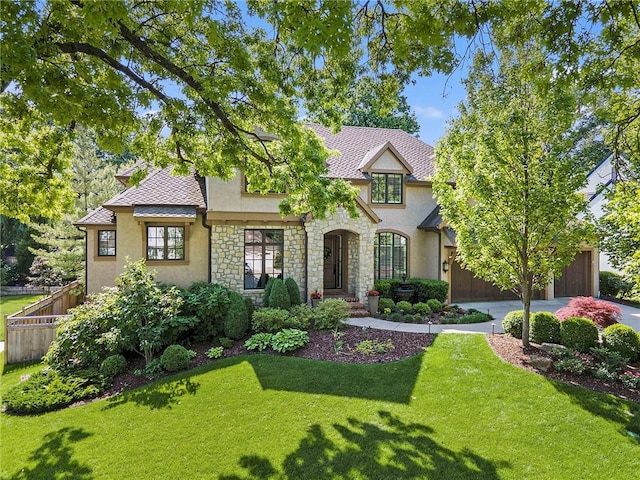 tudor-style house with stucco siding, stone siding, a garage, and driveway