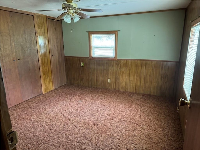 32572 Magnolia Ln, Excelsior Springs, MO 64024 - unfurnished bedroom with wooden walls, wainscoting, carpet flooring, multiple windows, and ceiling fan