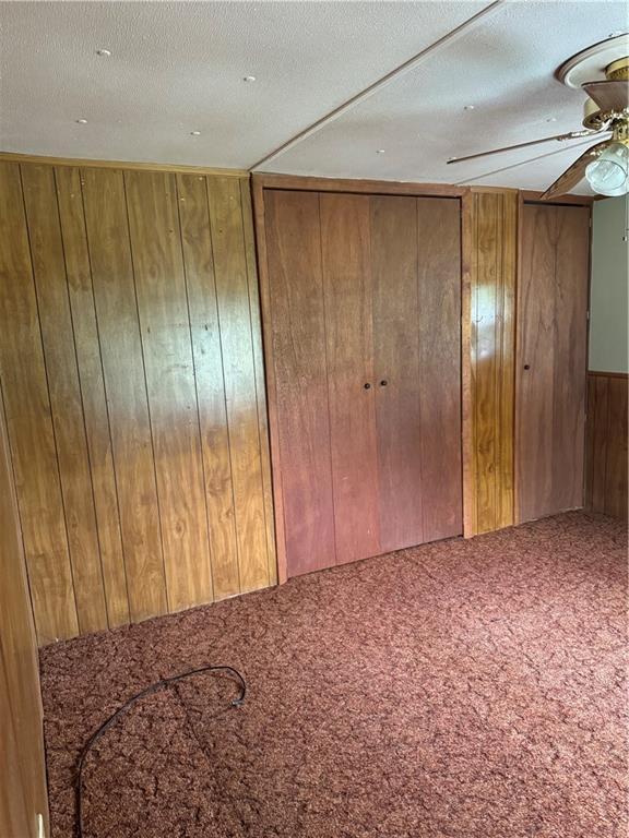 32572 Magnolia Ln, Excelsior Springs, MO 64024 - unfurnished bedroom with wood walls, carpet floors, a textured ceiling, and ceiling fan