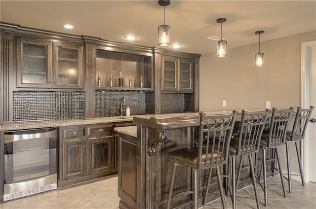 1110 Metfield Ln, Raymore, MO 64083 - indoor wet bar featuring wine cooler, decorative light fixtures, light tile patterned flooring, decorative backsplash, and recessed lighting