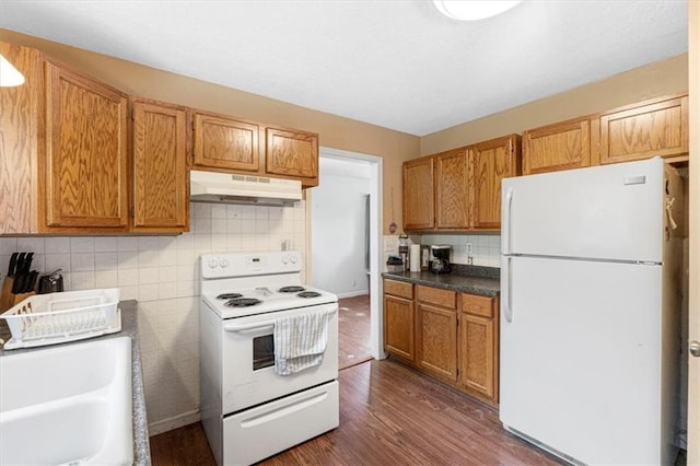 9021 E 79th St, Raytown, MO 64138 - kitchen with white appliances, under cabinet range hood, dark wood-type flooring, tasteful backsplash, and brown cabinetry