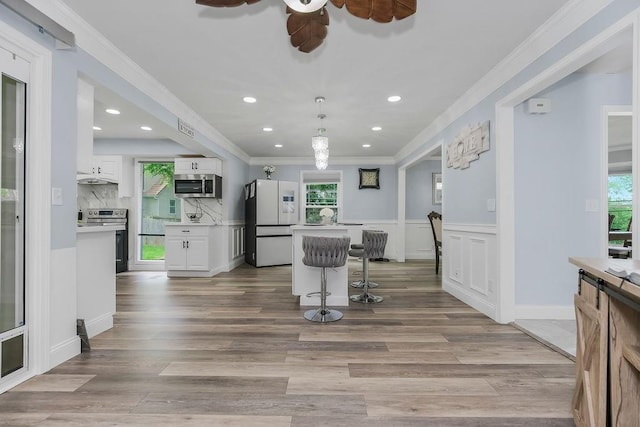 11506 Knox St, Overland Park, KS 66210 - kitchen featuring stainless steel appliances, ornamental molding, white cabinets, light countertops, and a breakfast bar
