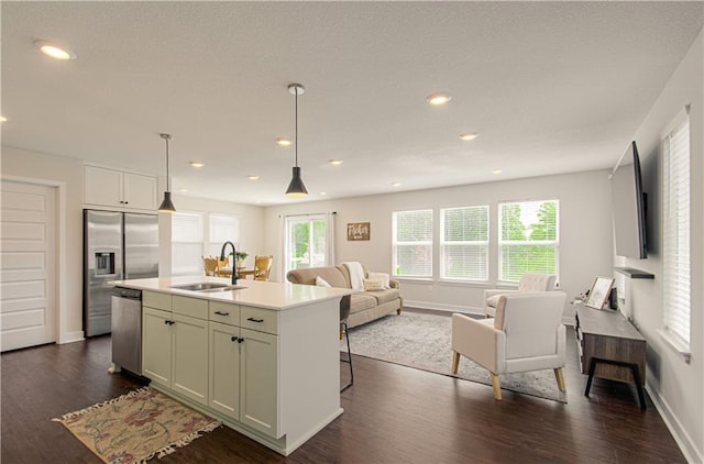 kitchen with a sink, stainless steel appliances, open floor plan, dark wood-style floors, and light countertops