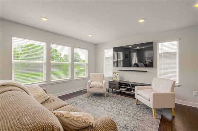 living area with baseboards, healthy amount of natural light, dark wood-style flooring, recessed lighting, and a textured ceiling