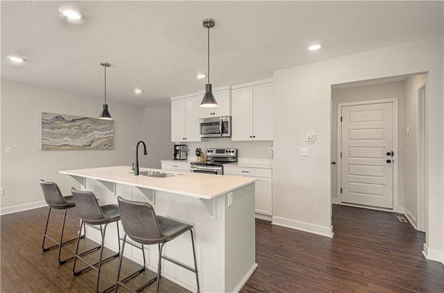 kitchen with stainless steel appliances, a sink, dark wood finished floors, an island with sink, and a breakfast bar area