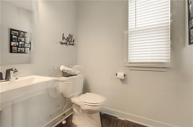 half bathroom with toilet, baseboards, wood finished floors, and a sink