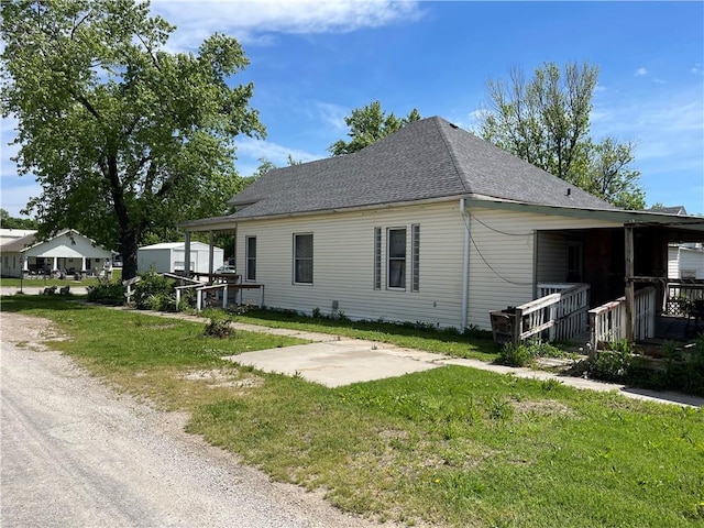 view of front of house featuring a patio, a front yard, and a shingled roof