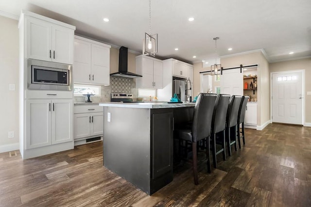 85 Birdie Ln, Mound City, KS 66056 - kitchen with wall chimney exhaust hood, appliances with stainless steel finishes, a barn door, ornamental molding, and dark wood finished floors