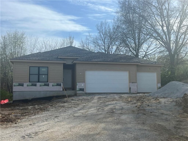 view of front of house featuring a garage, dirt driveway, and a shingled roof