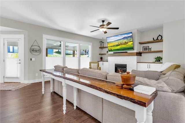 living area with dark wood finished floors, healthy amount of natural light, a ceiling fan, and a tiled fireplace