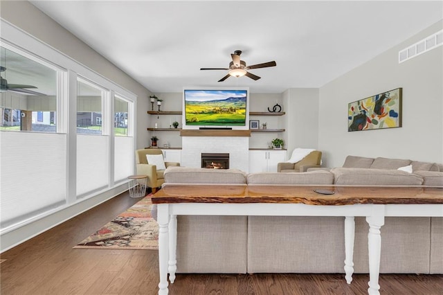 living room with a ceiling fan, a warm lit fireplace, and wood finished floors
